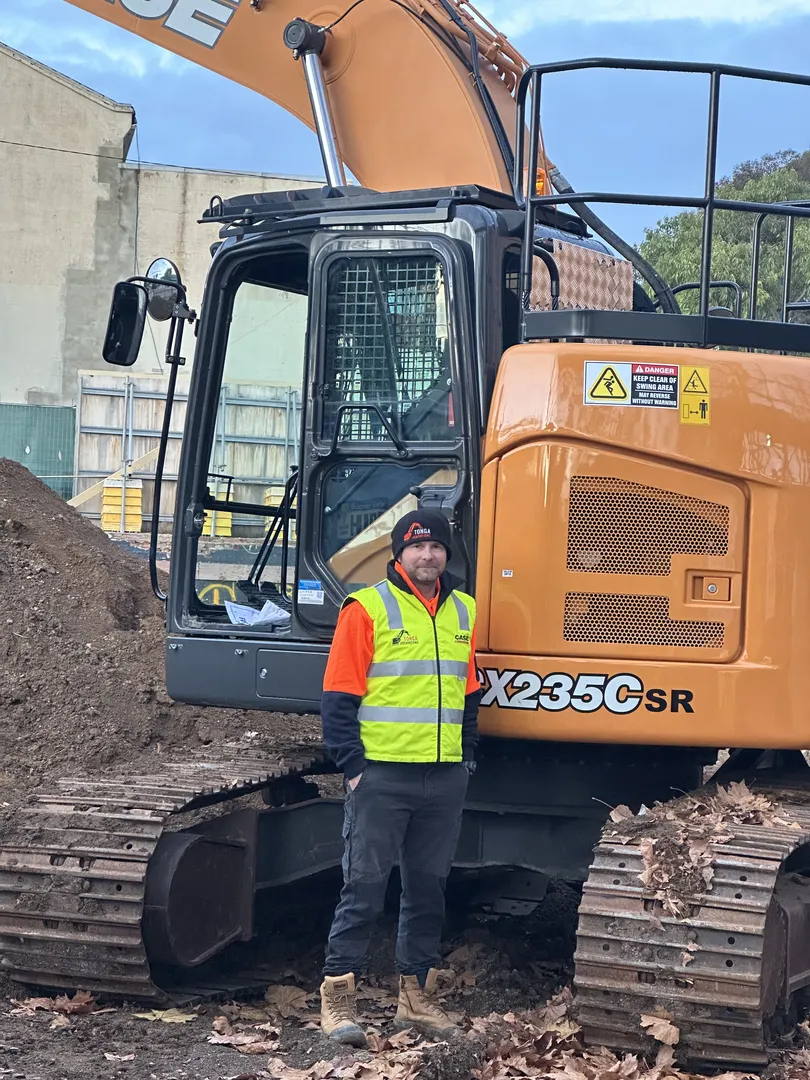 Construction worker standing by an excavator on site.